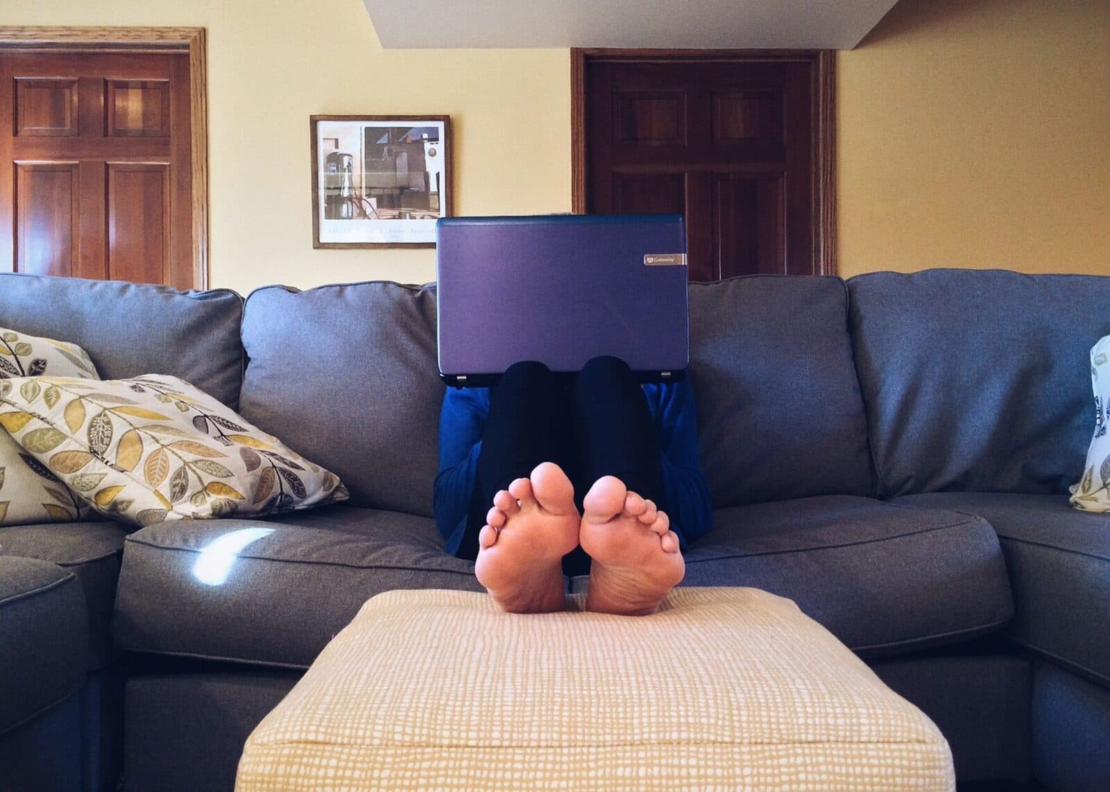 Person relaxing on a cozy couch with a laptop, embodying modern home comfort.