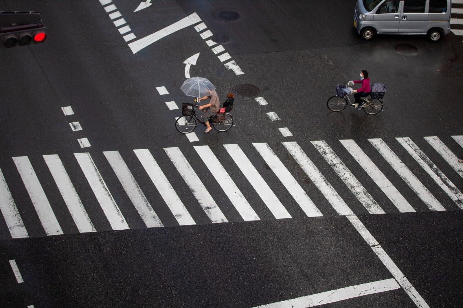 Cyclists navigate a rainy city crosswalk with umbrellas for protection.