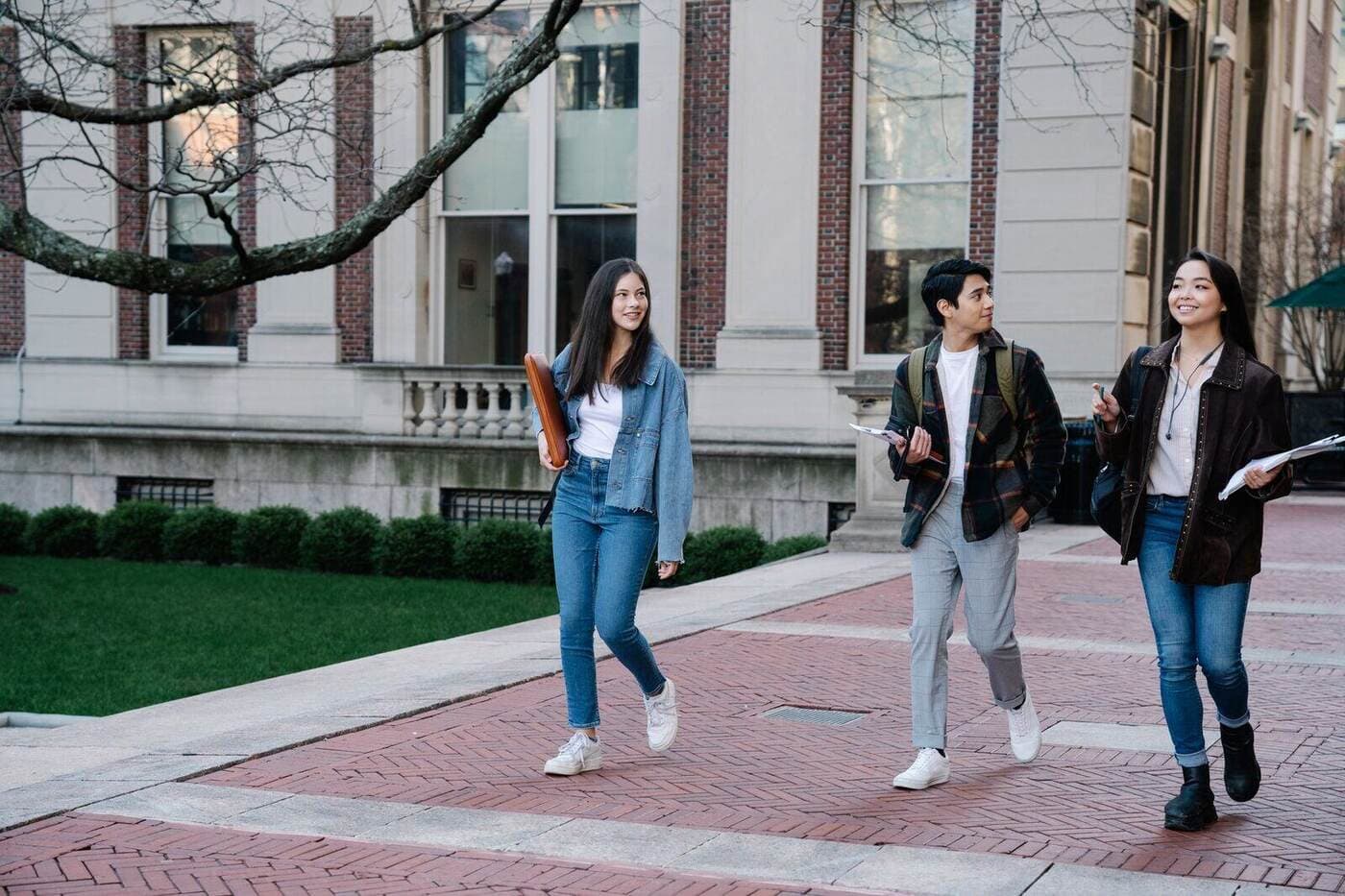 Group of young students walking on campus sidewalk on a bright day, showcasing casual university life.